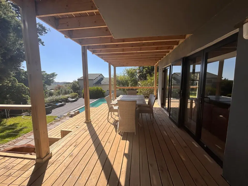 Covered timber deck with dining area overlooking a pool and garden