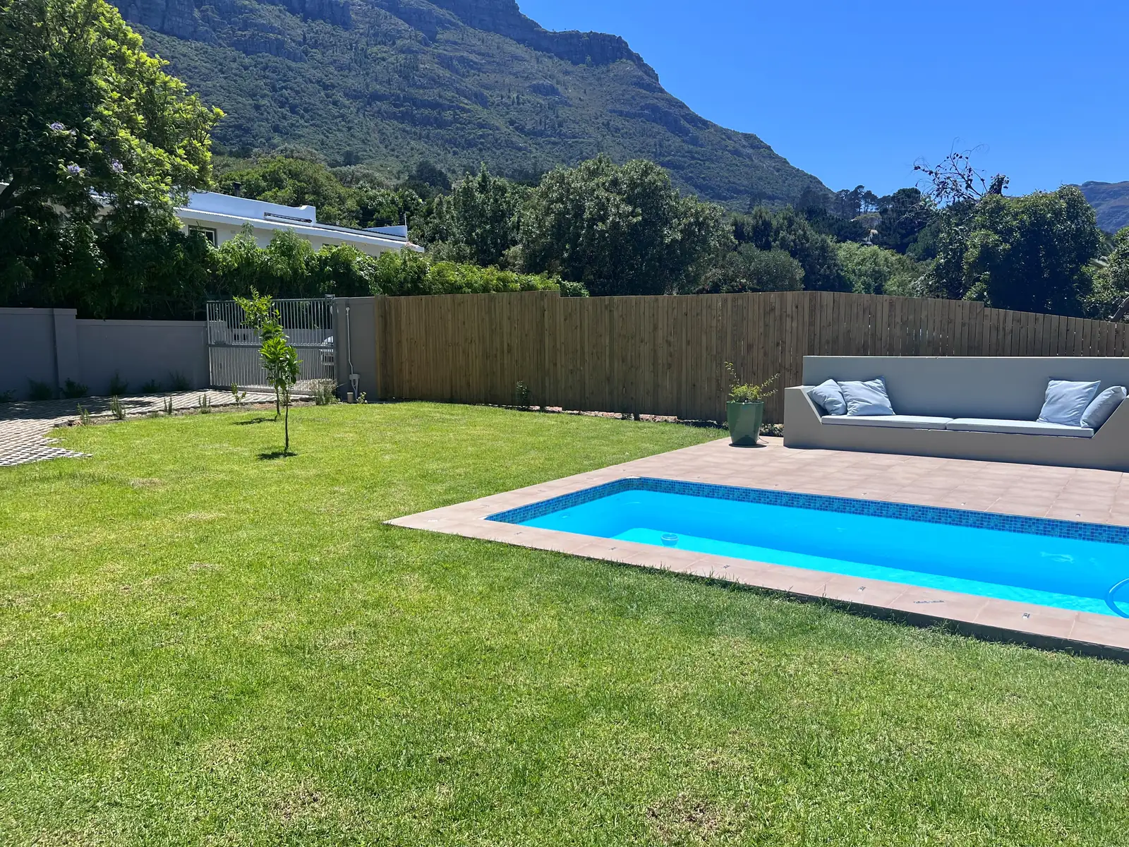 Lawn, swimming pool and timber boundary fence at a Cape Town home, with the mountain behind