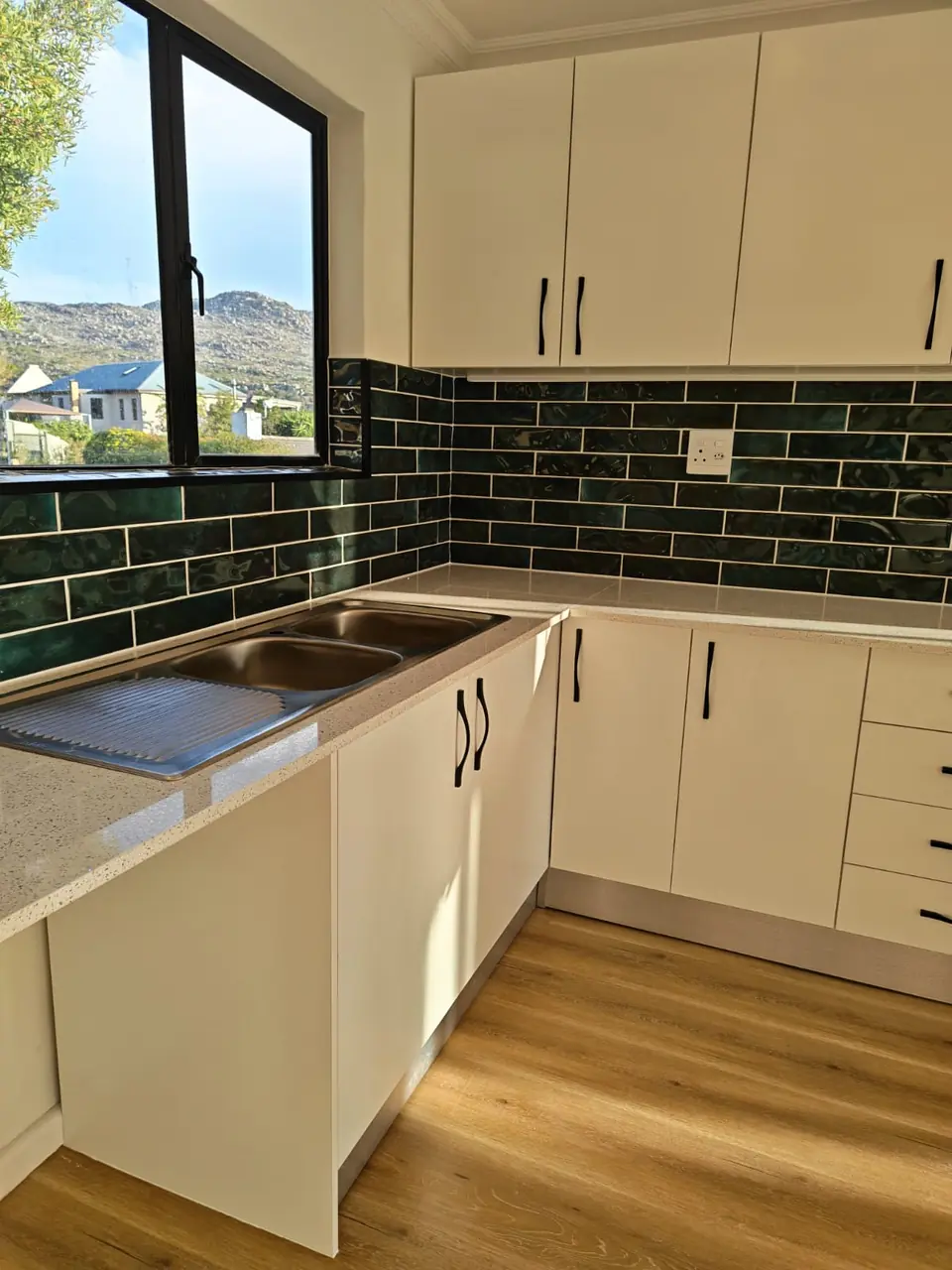 Kitchen corner with white cabinets, green subway tiles and a window