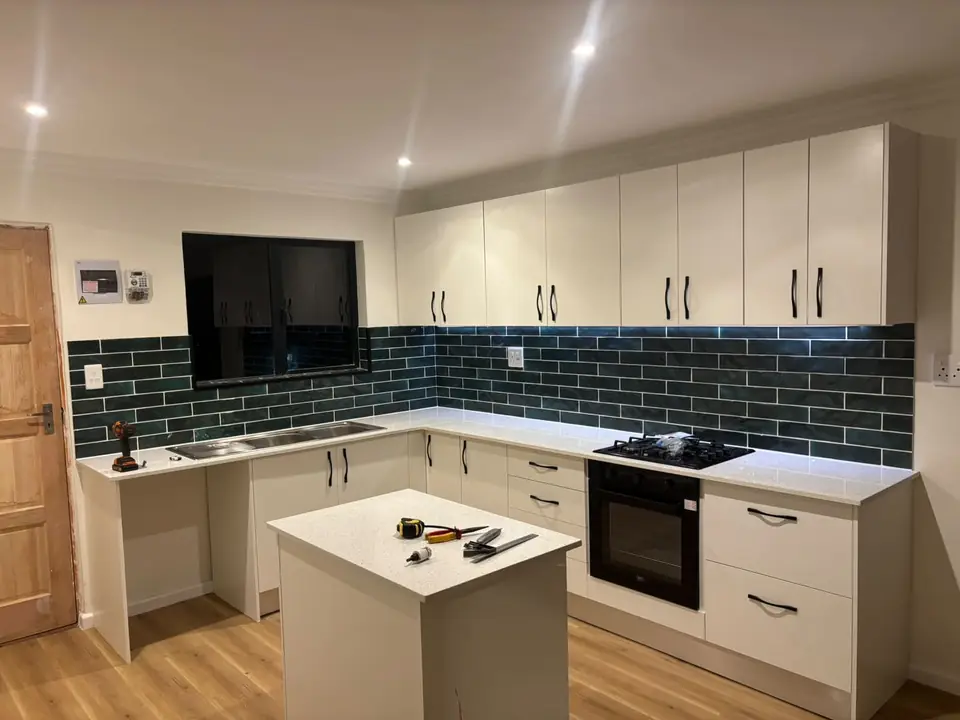 White kitchen with an island, black handles and dark green tiled splashback