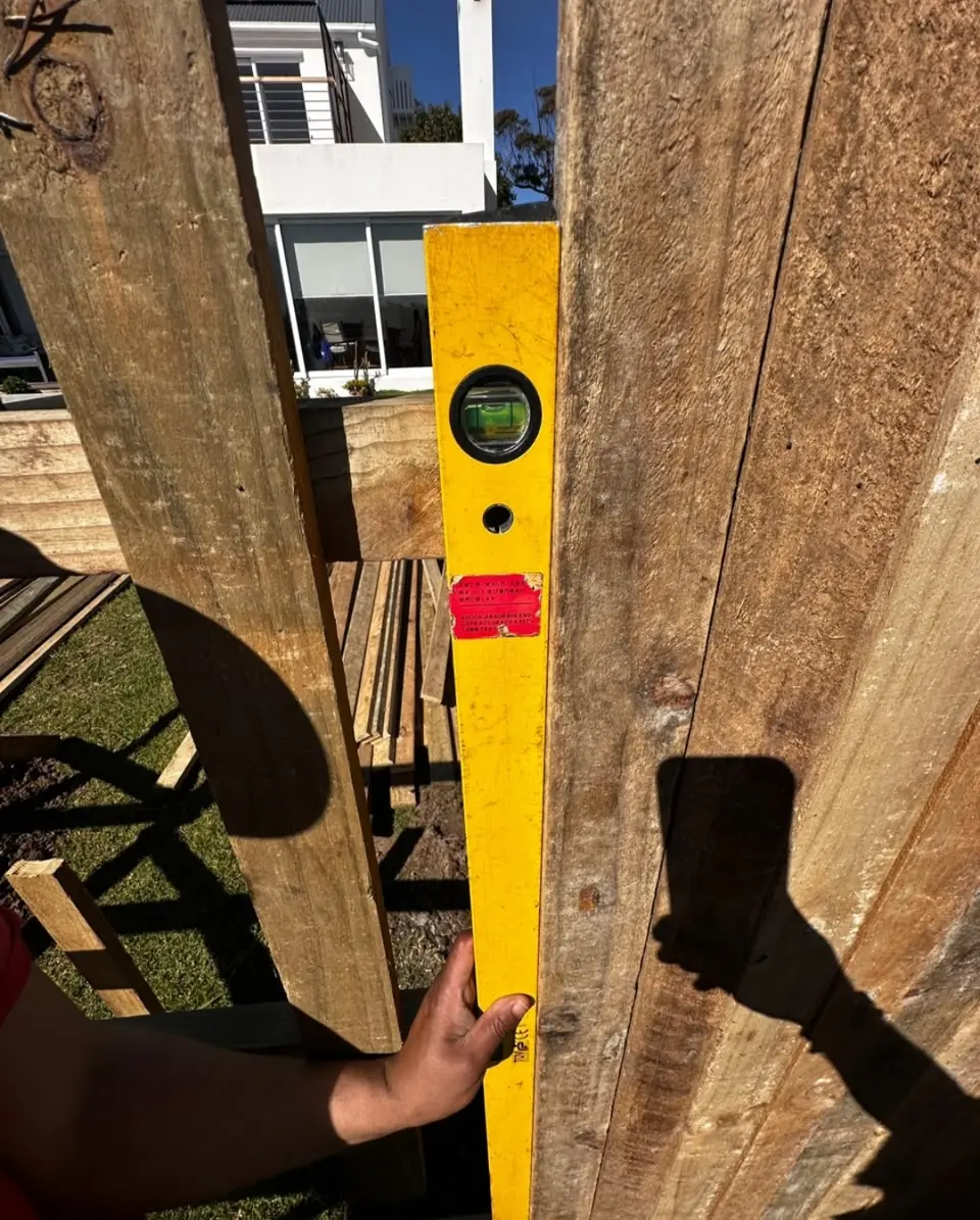 A spirit level held against a timber fence post during installation