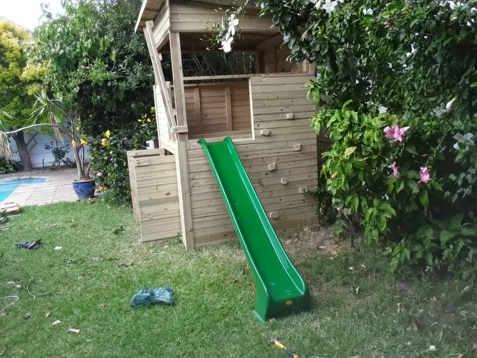 Timber jungle gym with a climbing wall, covered lookout and green slide on a garden lawn
